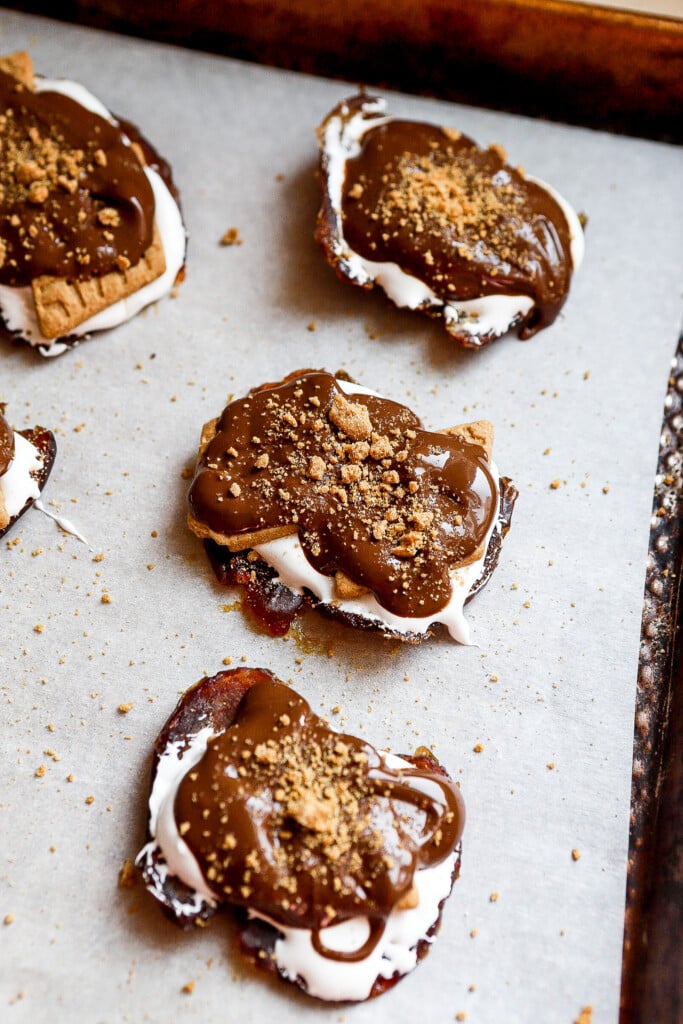 Smashed date s'mores on parchment topped with melted chocolate and crushed graham crackers