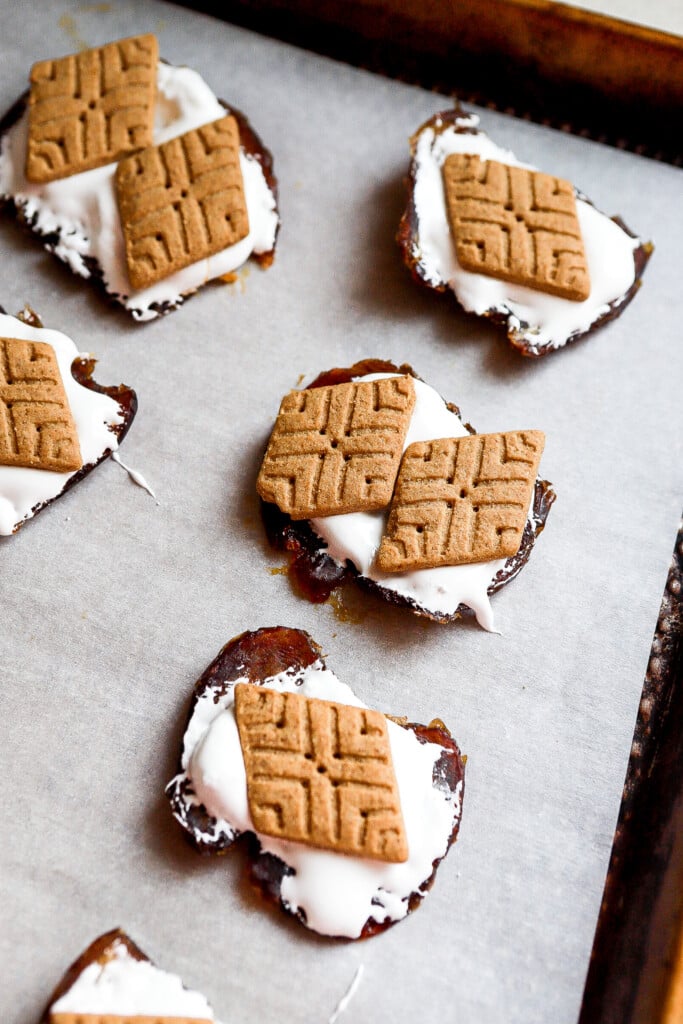 Marshmallow fluff spooned onto flattened Medjool dates on a sheet pan with sweet thins on top