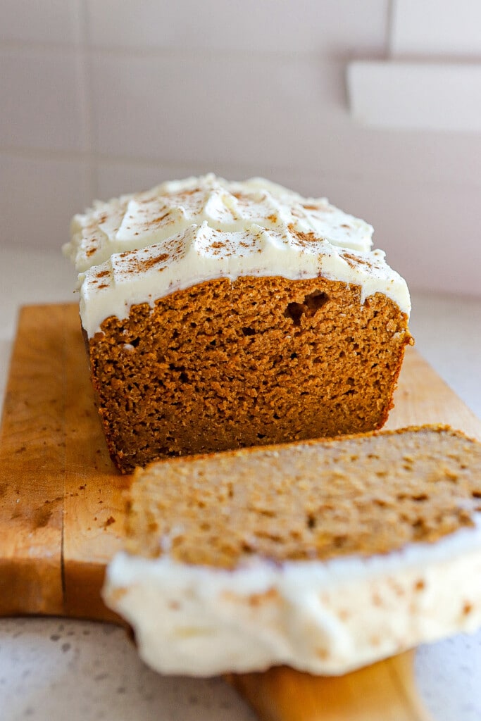 Sliced protein pumpkin bread with cream cheese frosting on a wooden board