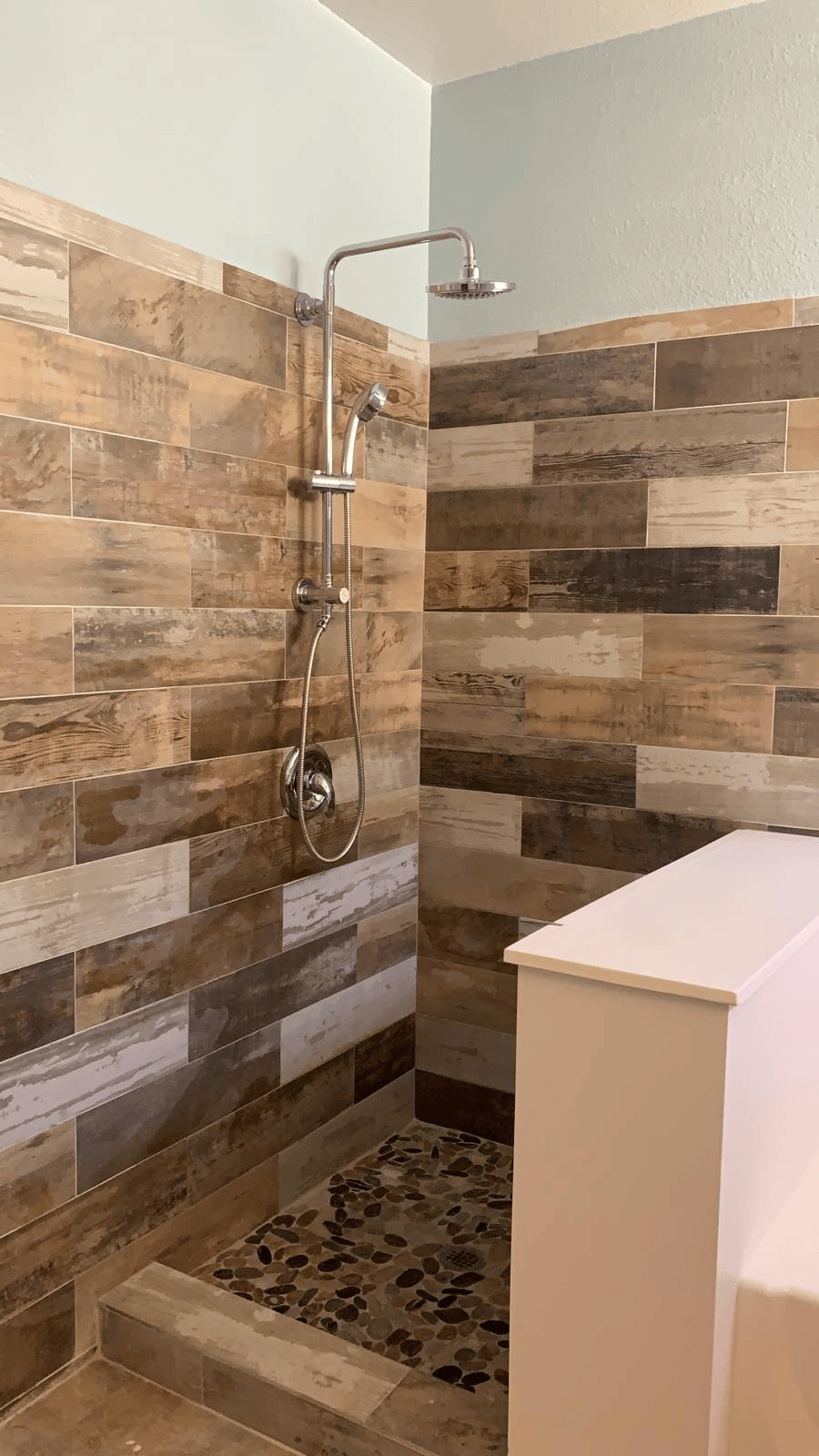 Finished Henderson shower remodel with wood-look wall tile, pebble floor and rainfall showerhead