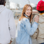 Teenage girl smiling while walking with two friends wearing hoodies and backpacks.