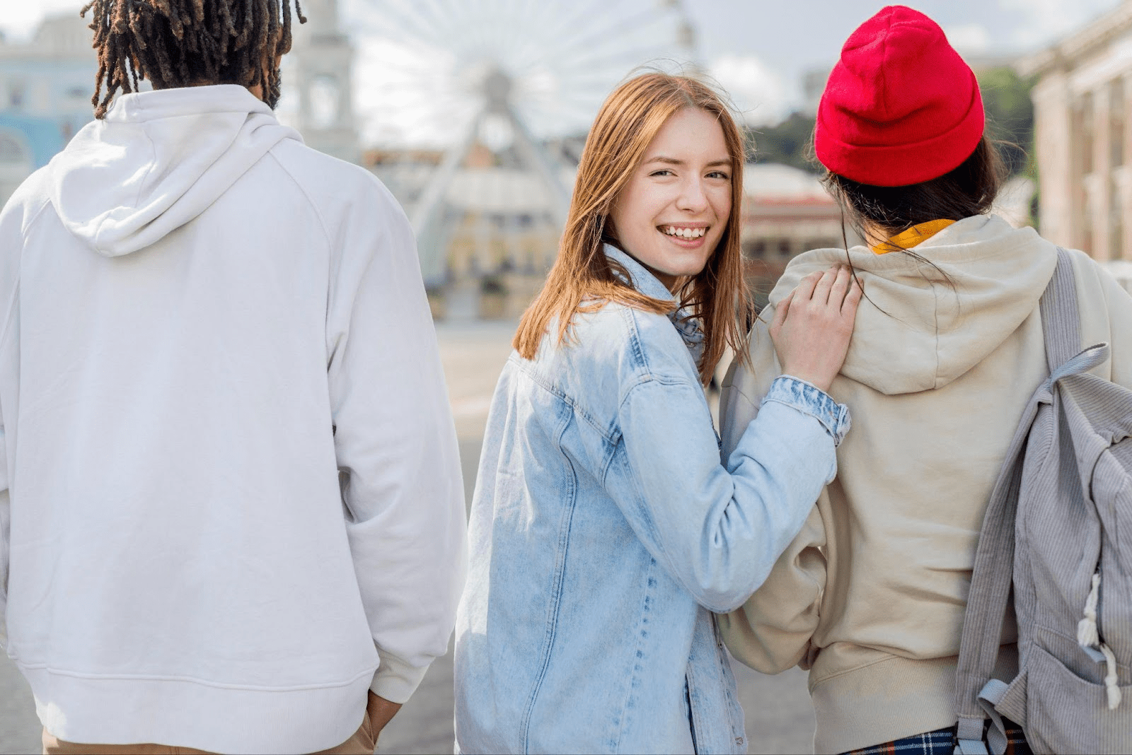 Teenage girl smiling while walking with two friends wearing hoodies and backpacks.