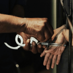 Hands in handcuffs behind back against prison bars.
