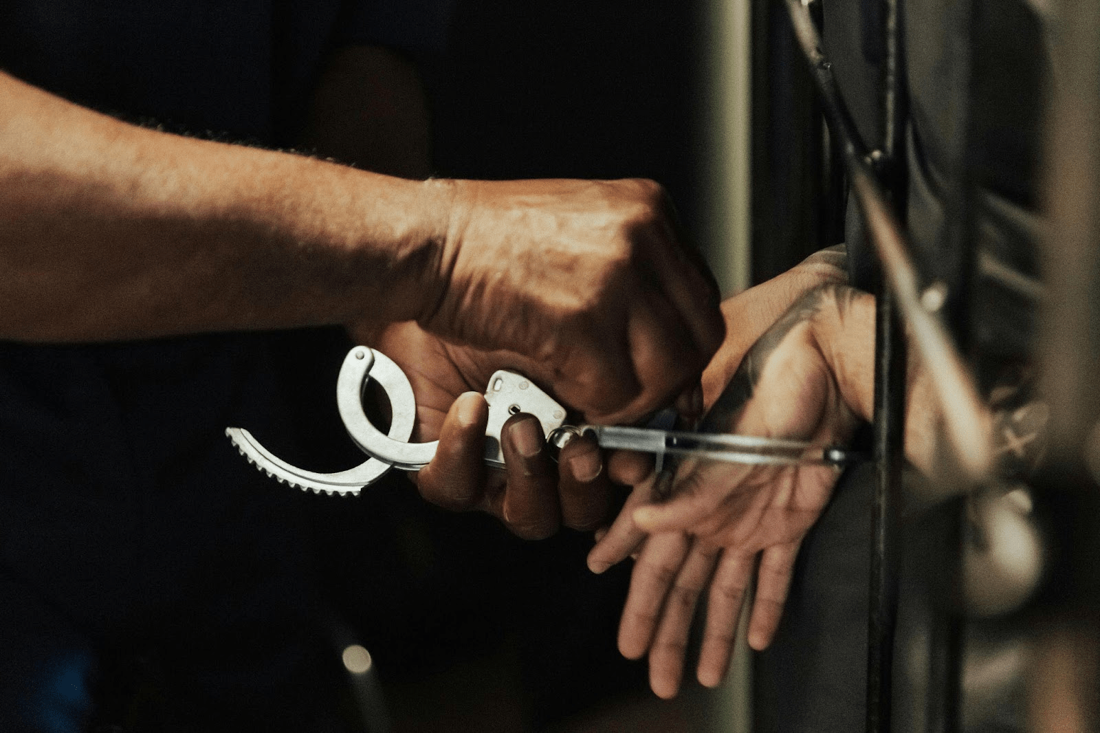 Hands in handcuffs behind back against prison bars.