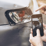 Person photographing car damage with smartphone for insurance claim documentation after accident in Alabama.