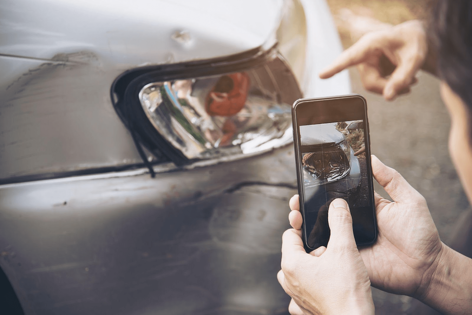 Person photographing car damage with smartphone for insurance claim documentation after accident in Alabama.