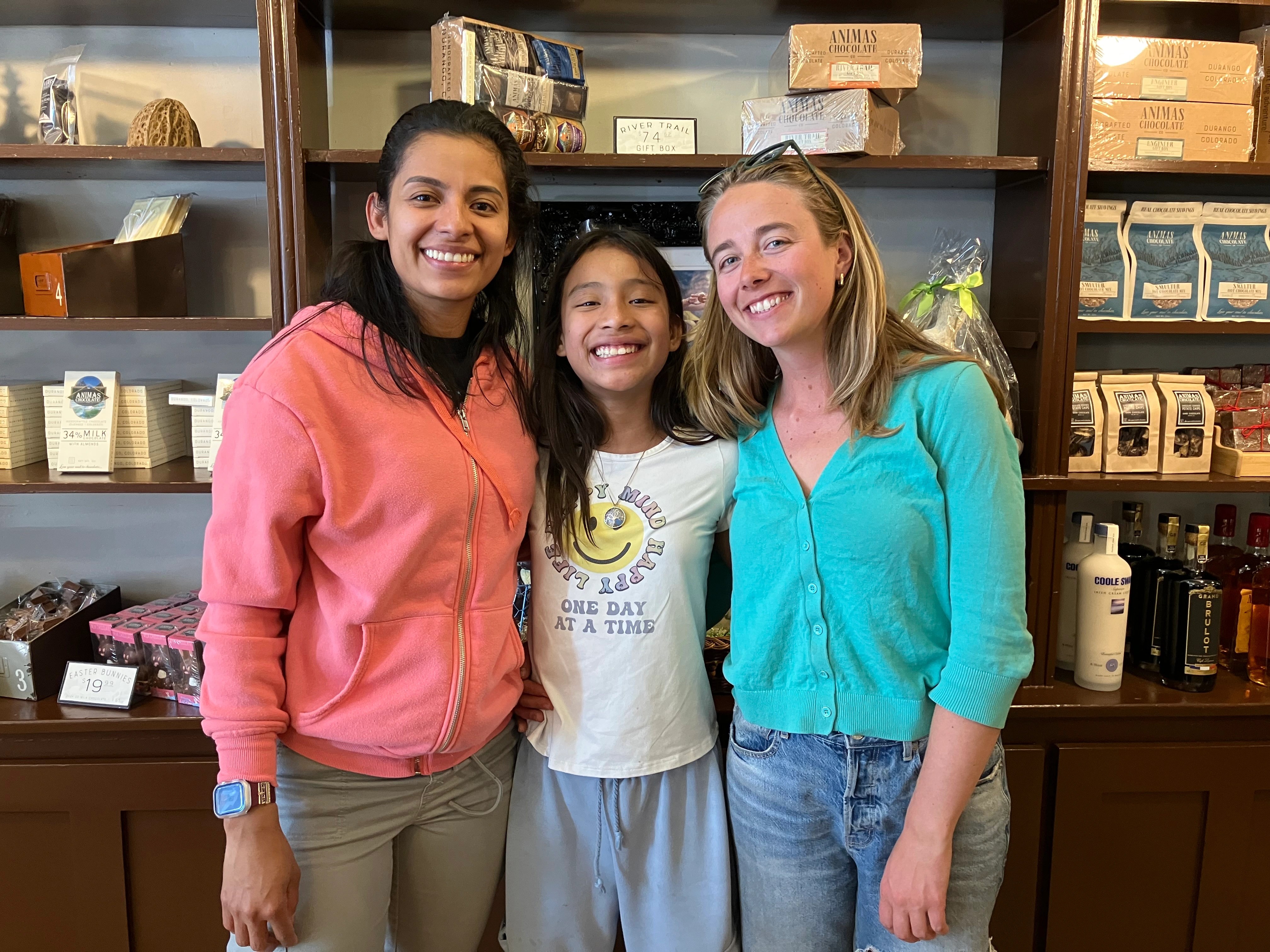Two Bigs and a Little standing together inside a local shop with shelves of goods behind them.