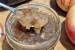 A jar of spiced apple jam with a spoonful of jam held over top with two apples barely visible off to the right side.