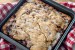 A pan of Apple cinnamon cake on a red and white checkered towel with an apple barely visible behind it.