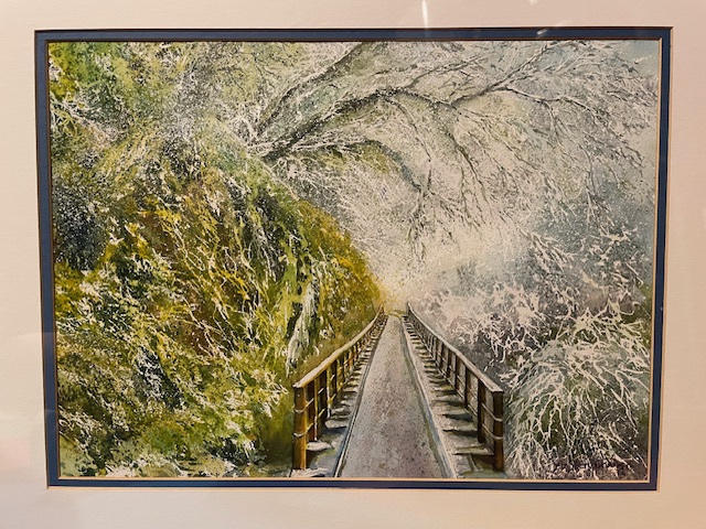 A watercolor painting of a straight wooden footbridge with railings extending forward through a frosty landscape. Frost-dusted tree branches form an arch overhead, while a steep bank covered in moss and snow borders the left side.