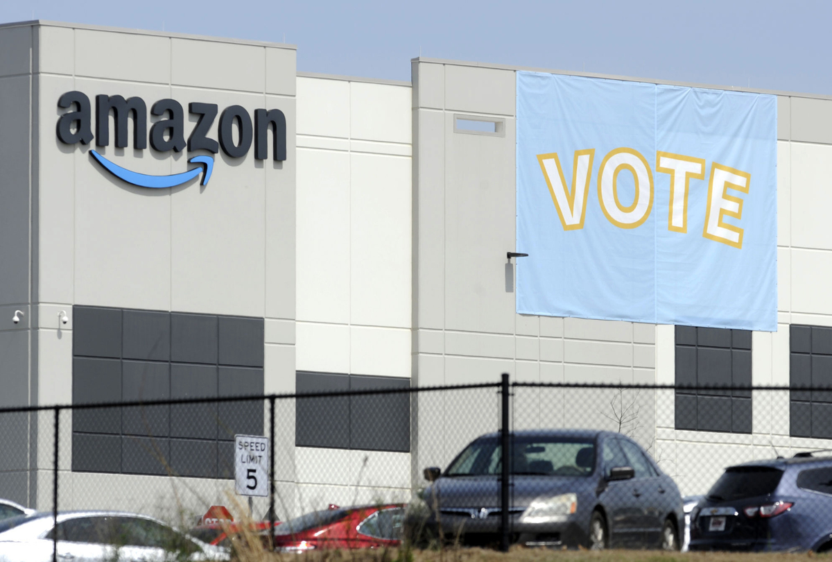 A banner reading "vote" hangs outside an Amazon warehouse.