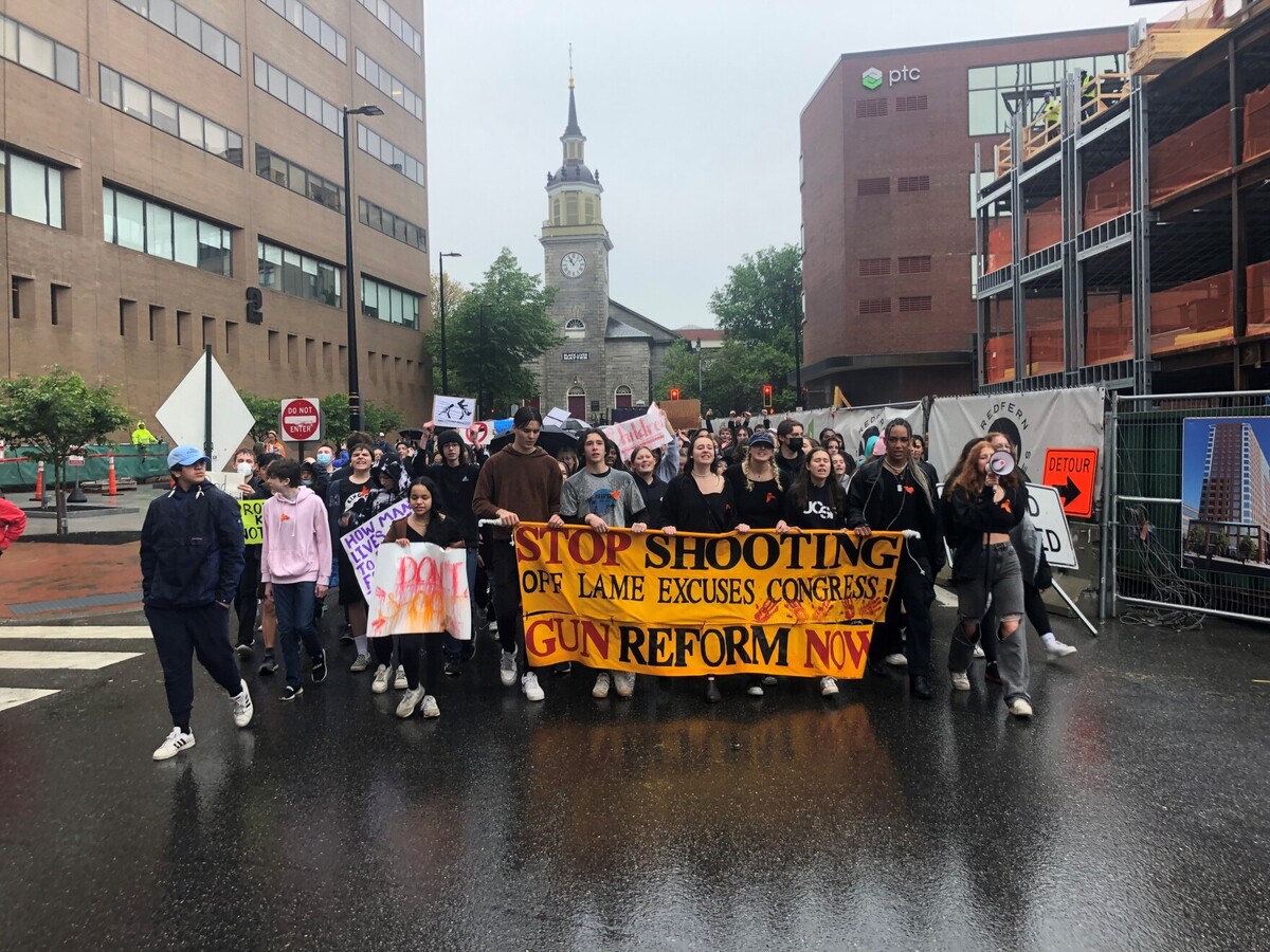 Students march in the rain carrying a banner demanding action on gun control.