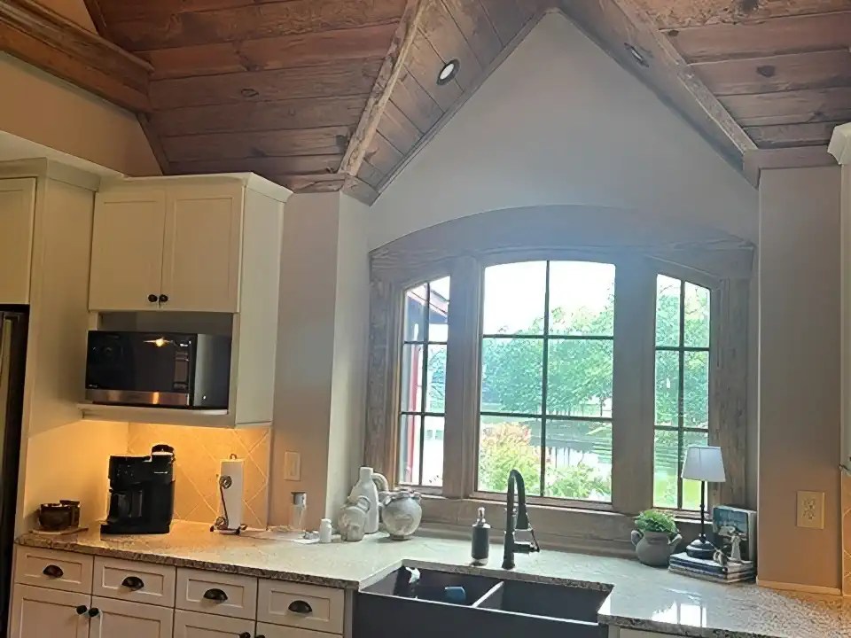 Farmhouse sink beneath an arched window under a dormered wood ceiling