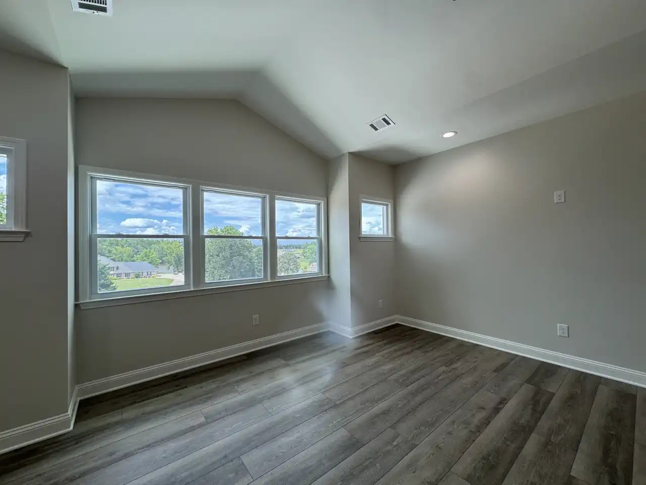Empty bonus room with vaulted ceiling and large windows overlooking trees