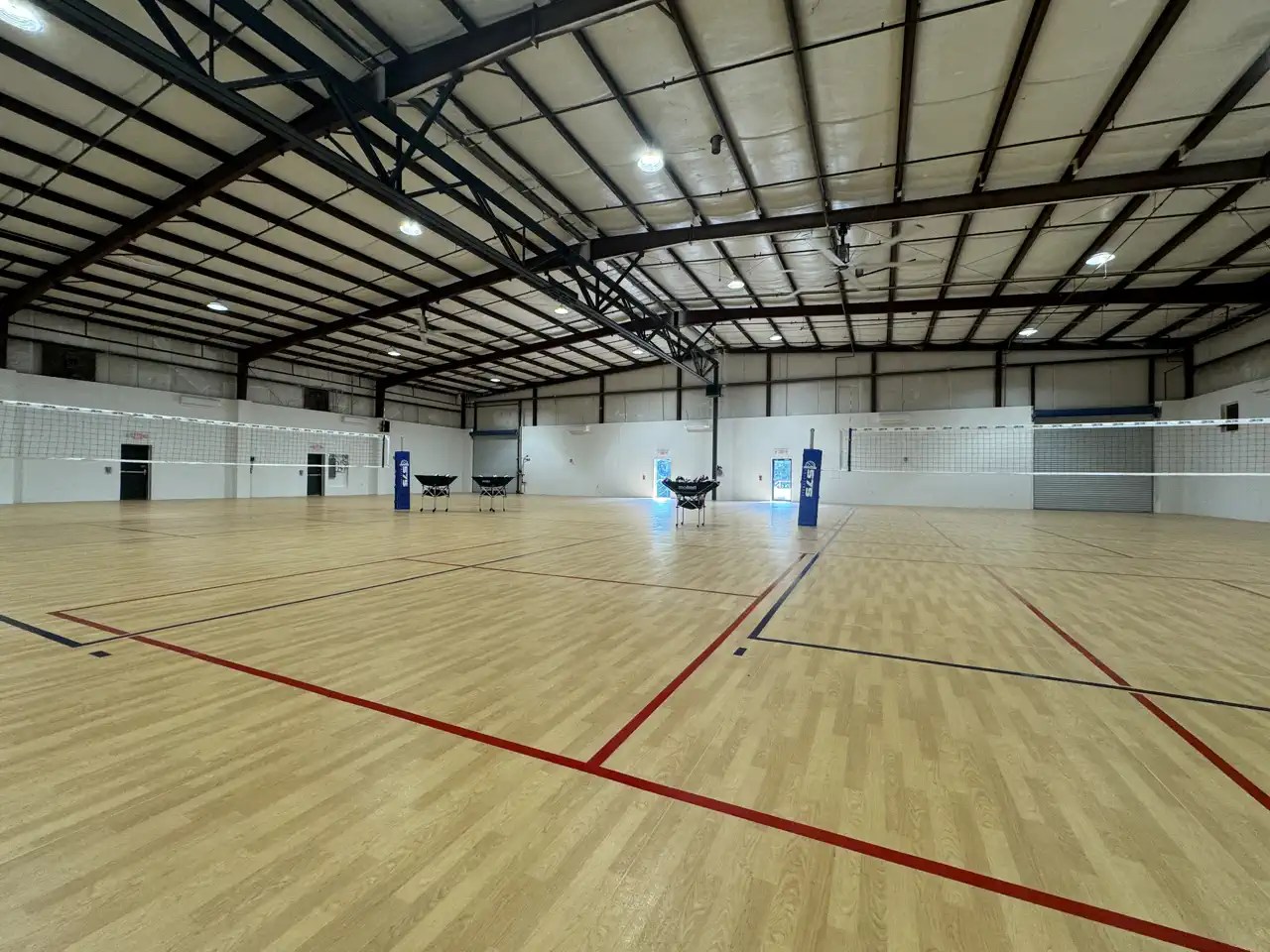 Empty indoor volleyball court with hardwood-style flooring and multiple nets