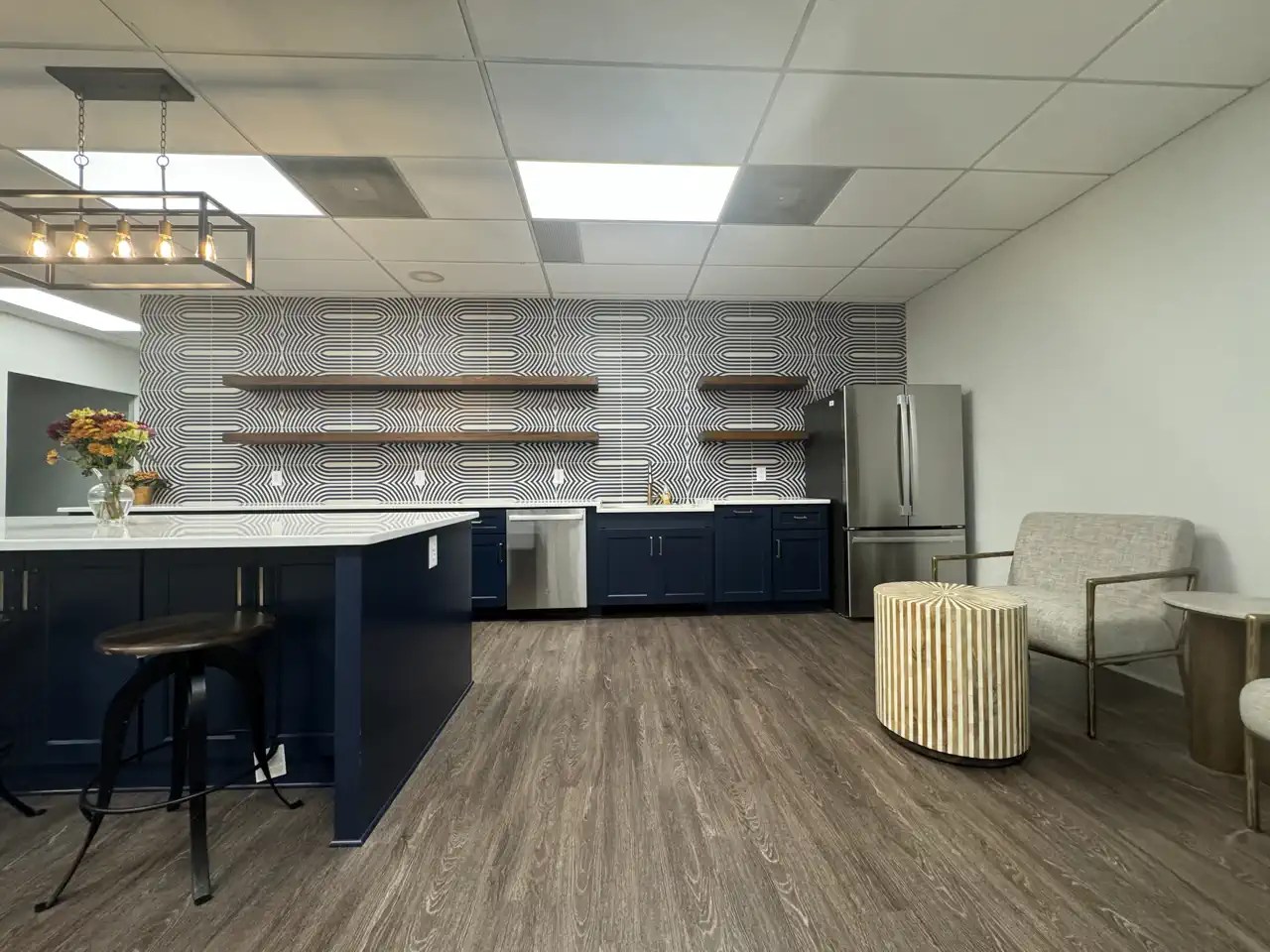 Office break room with navy cabinetry, patterned tile backsplash, and seating area