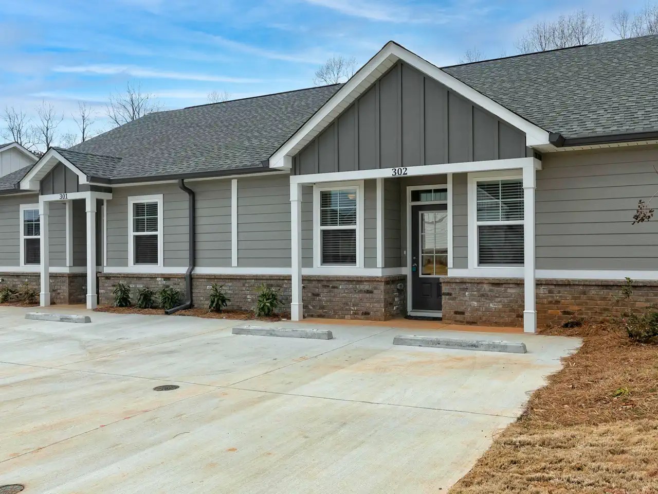 Gray townhome duplex with brick base, covered entries, and parking spaces
