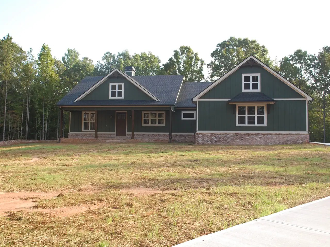 Dark green craftsman-style home with covered porch, set against a wooded backdrop