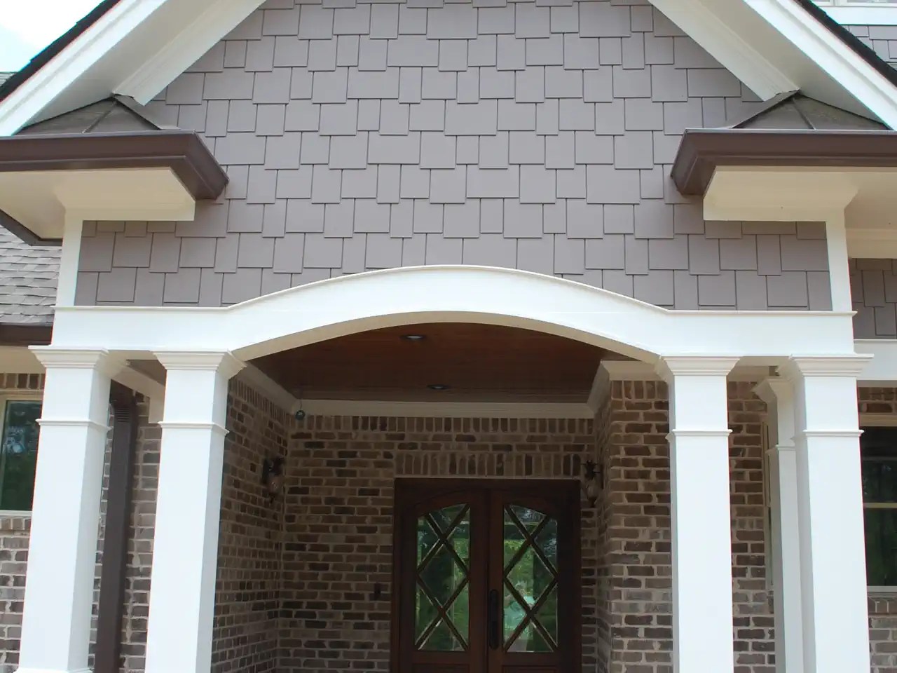 Covered entry with double wood doors, brick columns, and an arched gable roof