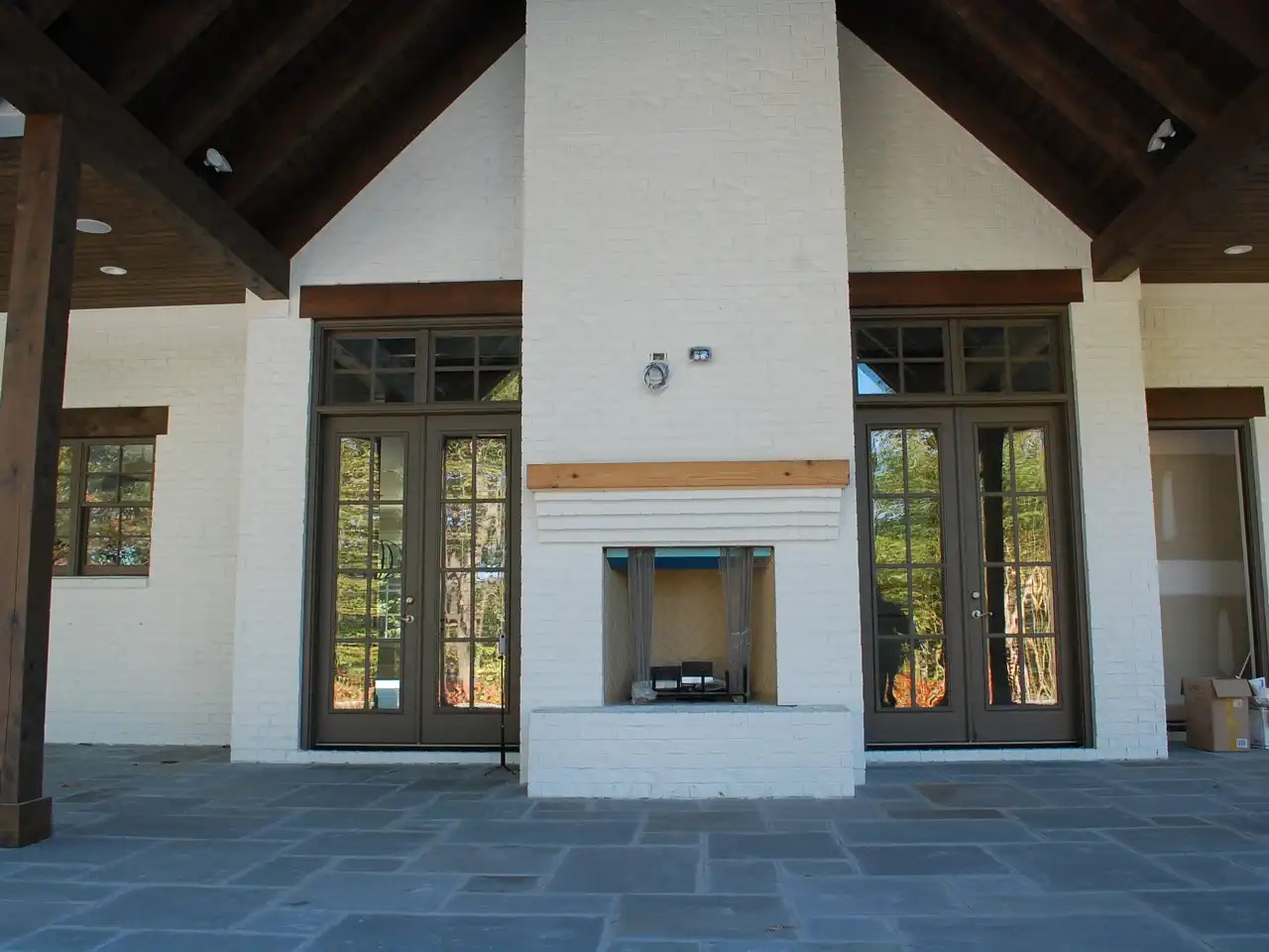 Covered patio with white brick fireplace, wood beam header, and French doors on either side