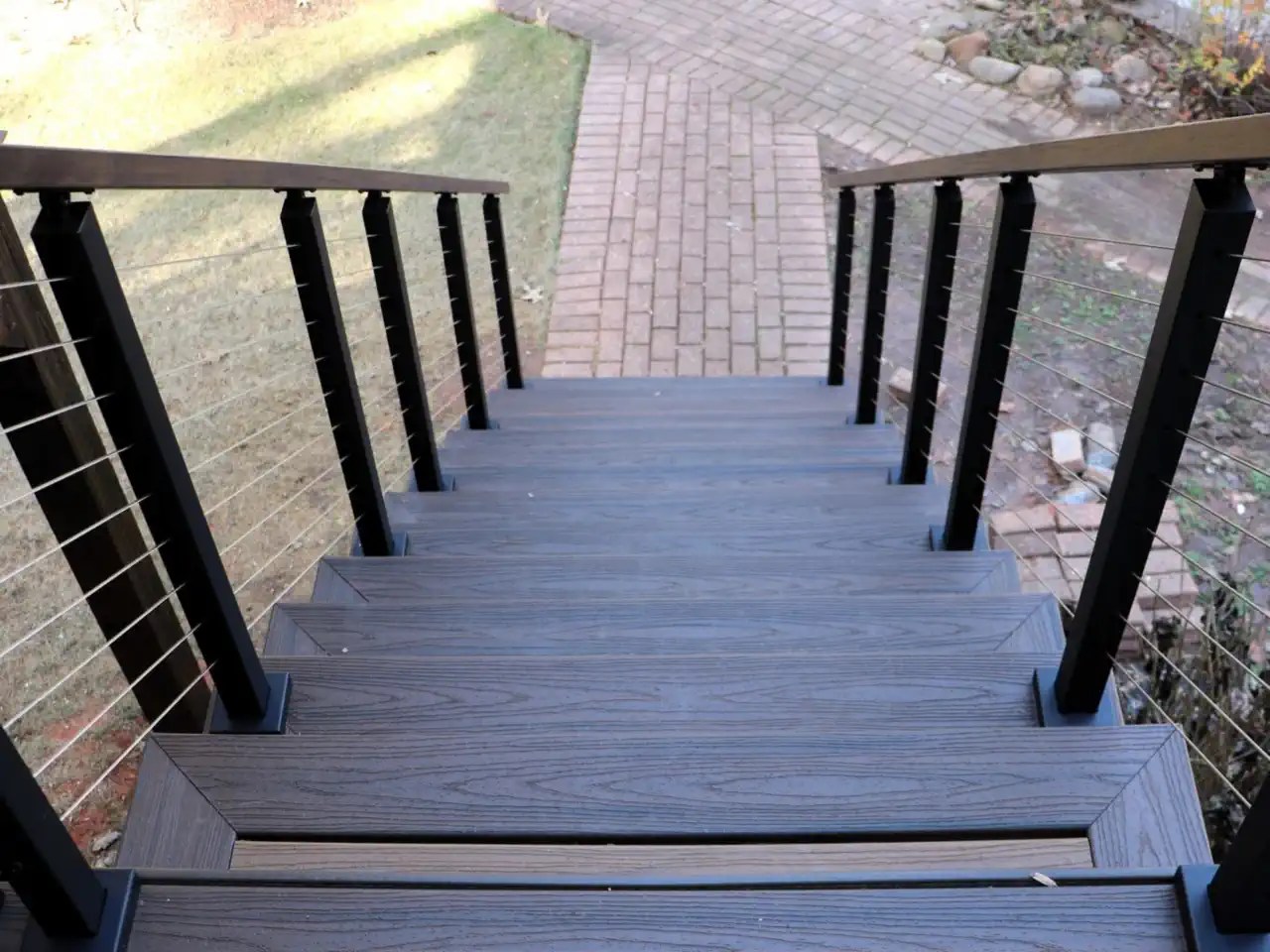 Composite deck stairs with black cable railing leading down to a pool