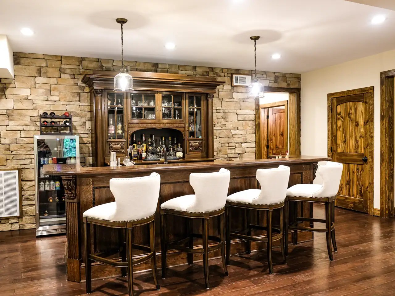 Basement bar with antique wood hutch, stone accent wall, and cream barstools