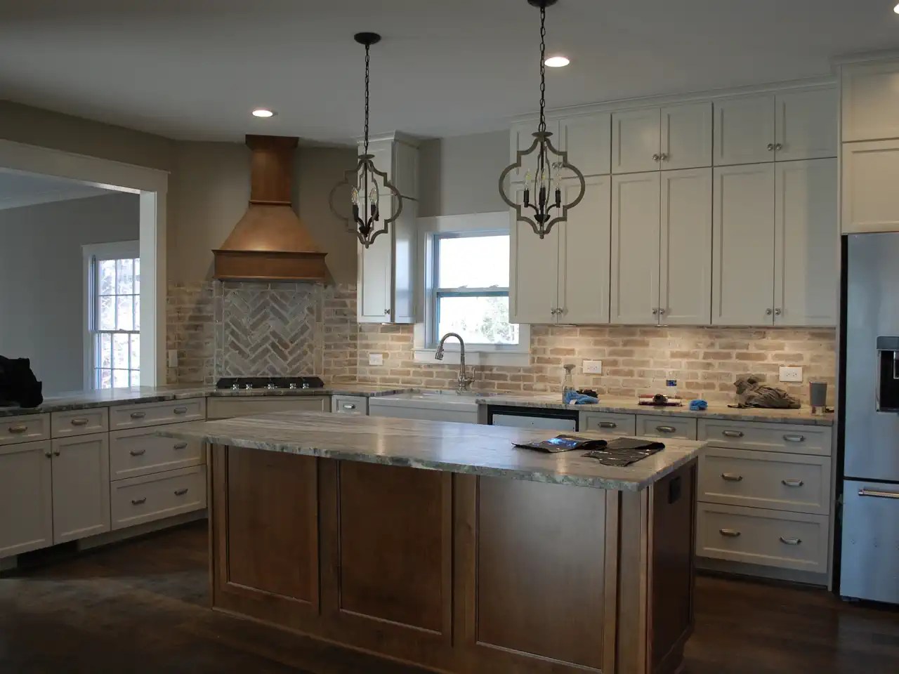 Kitchen with brick herringbone backsplash, copper range hood, and stone island