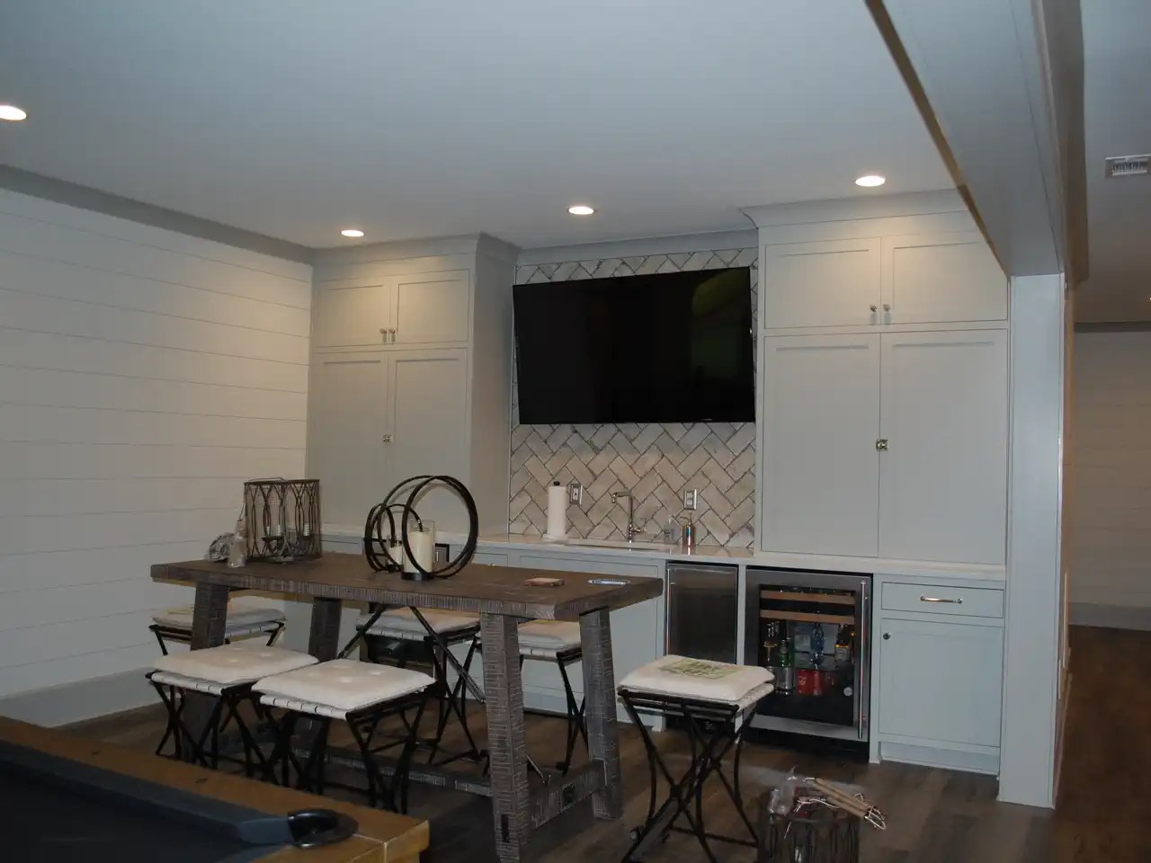 Basement bar with built-in cabinetry, wall-mounted TV, and high-top table seating