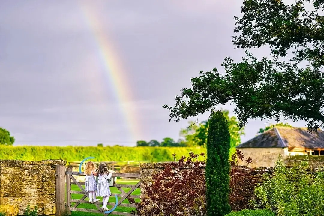 Happy children stood on a farm gate looking at a rainbow