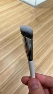 Abbildung eines angewinkelten Pinsels, der die Form der Fingerspitzen nachahmt. Dieser Pinsel eignet sich für präzise Anwendung und Verblendung, insbesondere in Bereichen, die mehr Kontrolle oder einen spezifischen Winkel erfordern, wie z. B. die Lidfalte oder entlang der Wangenknochen. Die schräge Form ermöglicht Vielseitigkeit bei der Anwendung und erleichtert das Erreichen verschiedener Gesichtsbereiche mit Präzision.