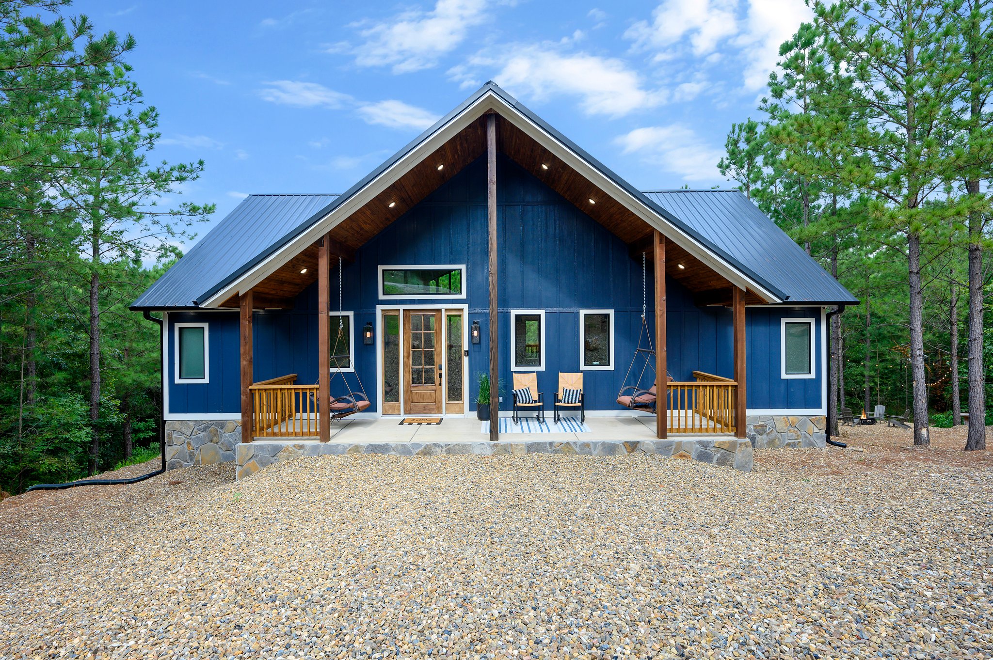Beautiful blue cabin with porch swing-chairs surrounded by pine trees.