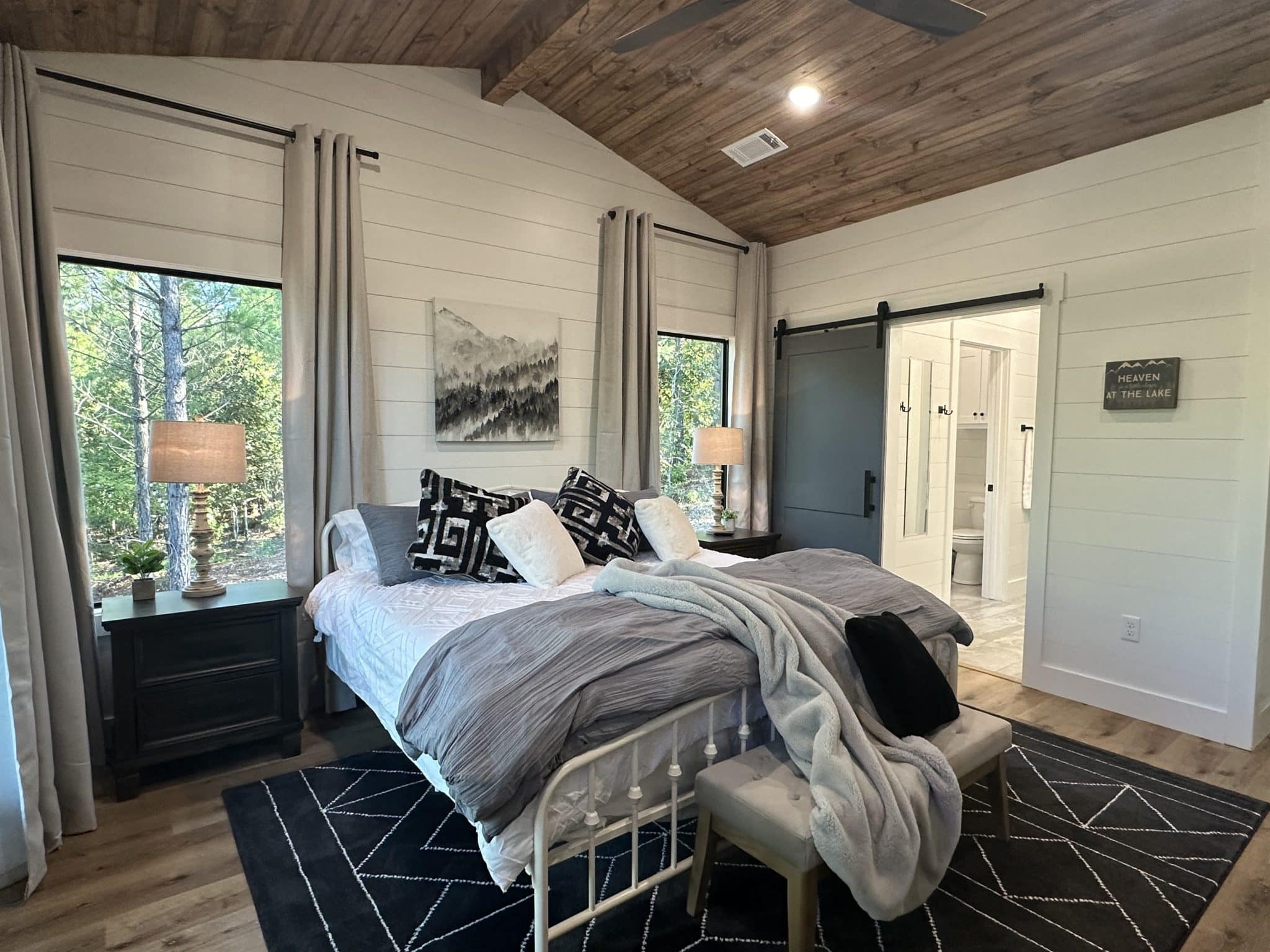 King bedroom with vaulted wood ceiling, forest-view windows, and en-suite bathroom