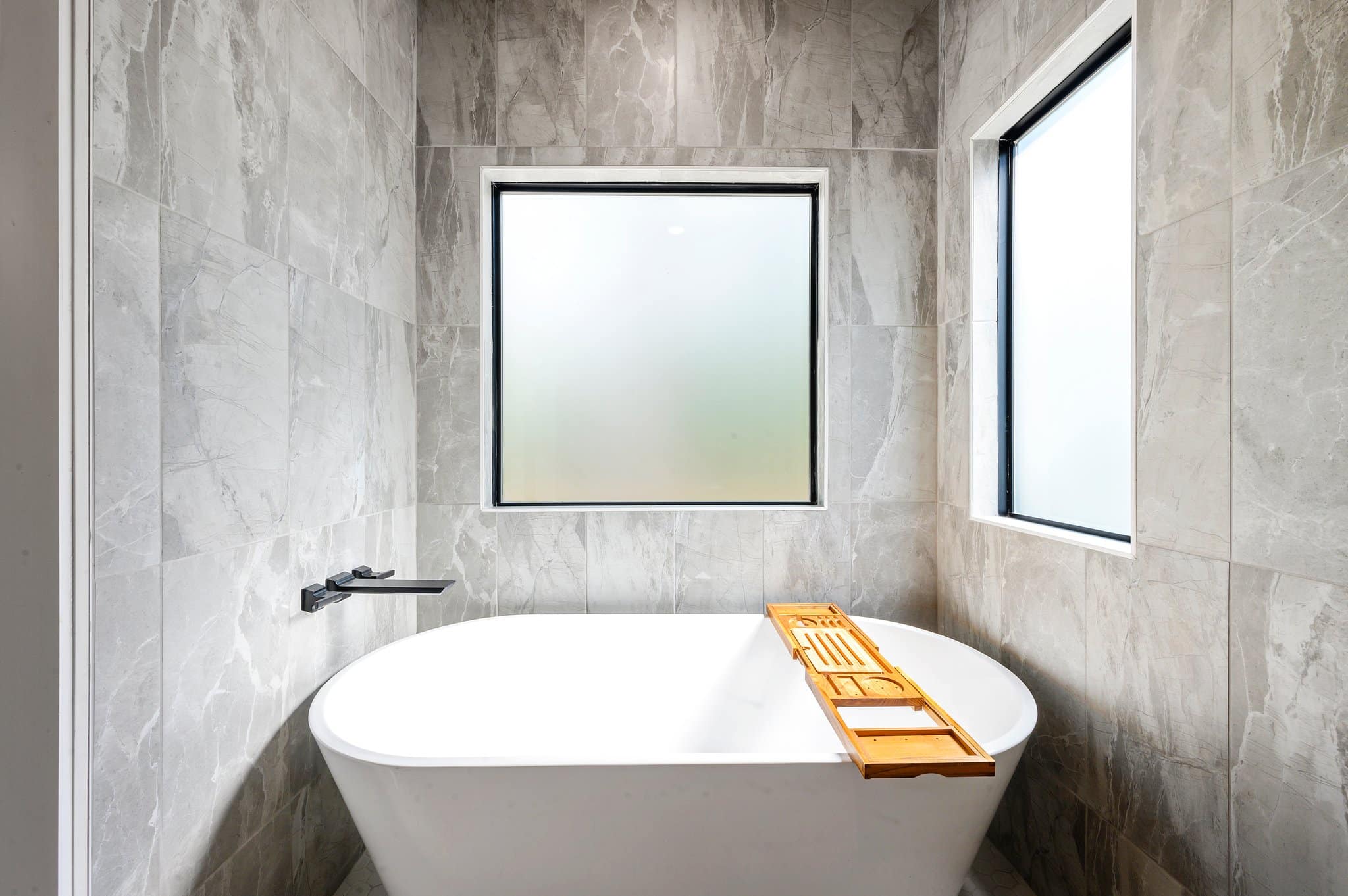 Freestanding soaking tub surrounded by light marble tile