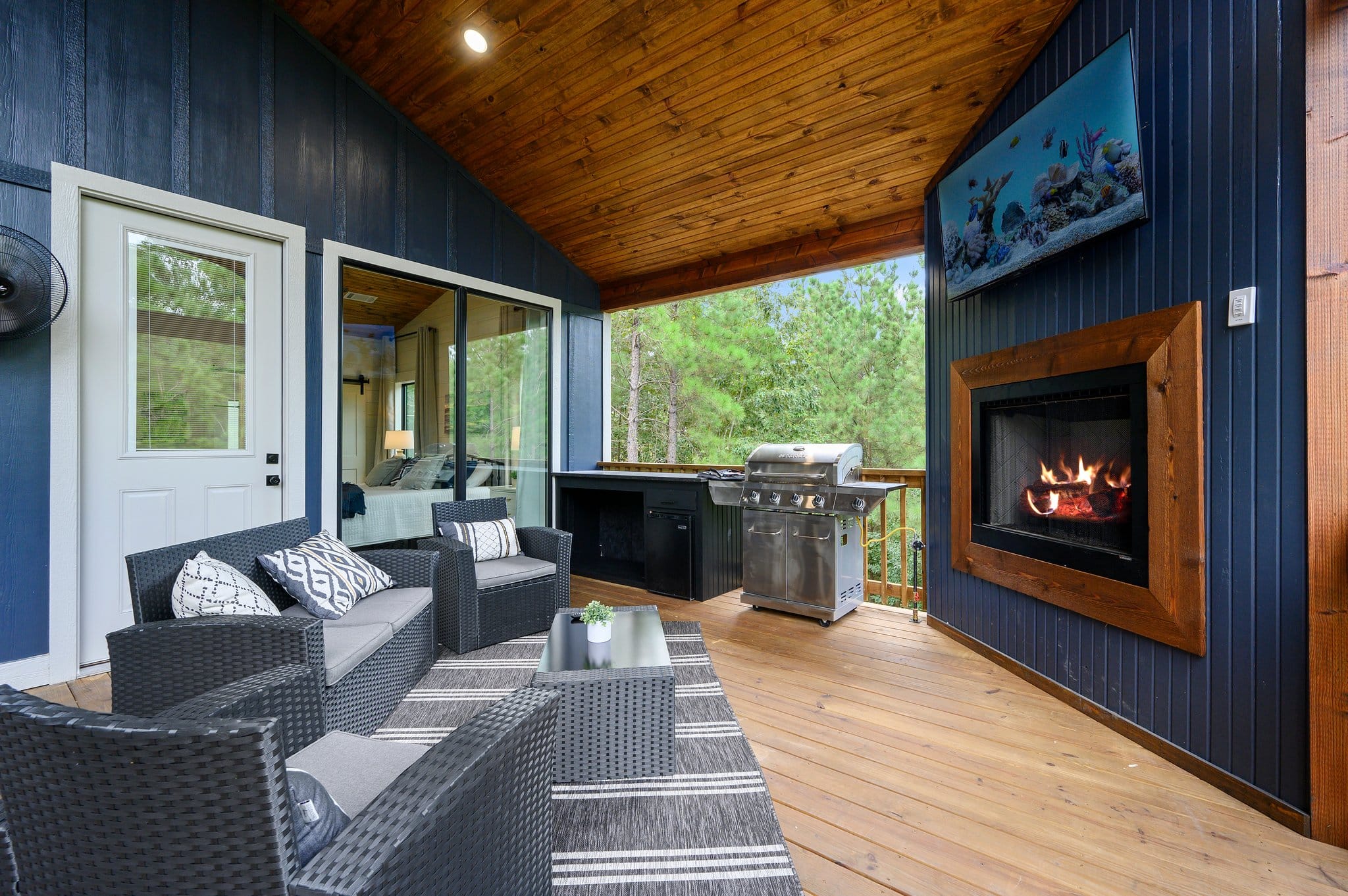 Covered outdoor living area with wicker seating, fireplace, television, and grill