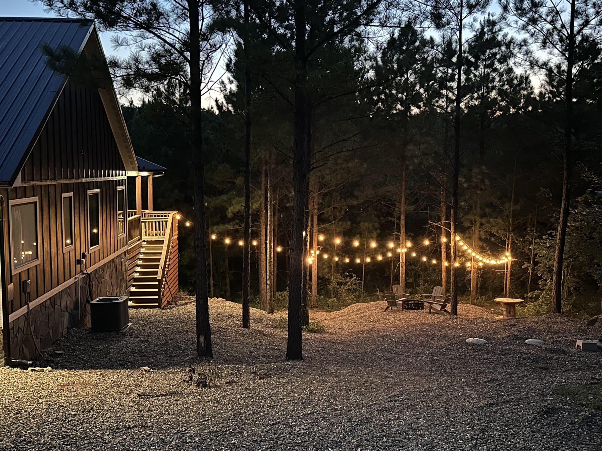 Cabin and wooded outdoor area illuminated by string lights at dusk