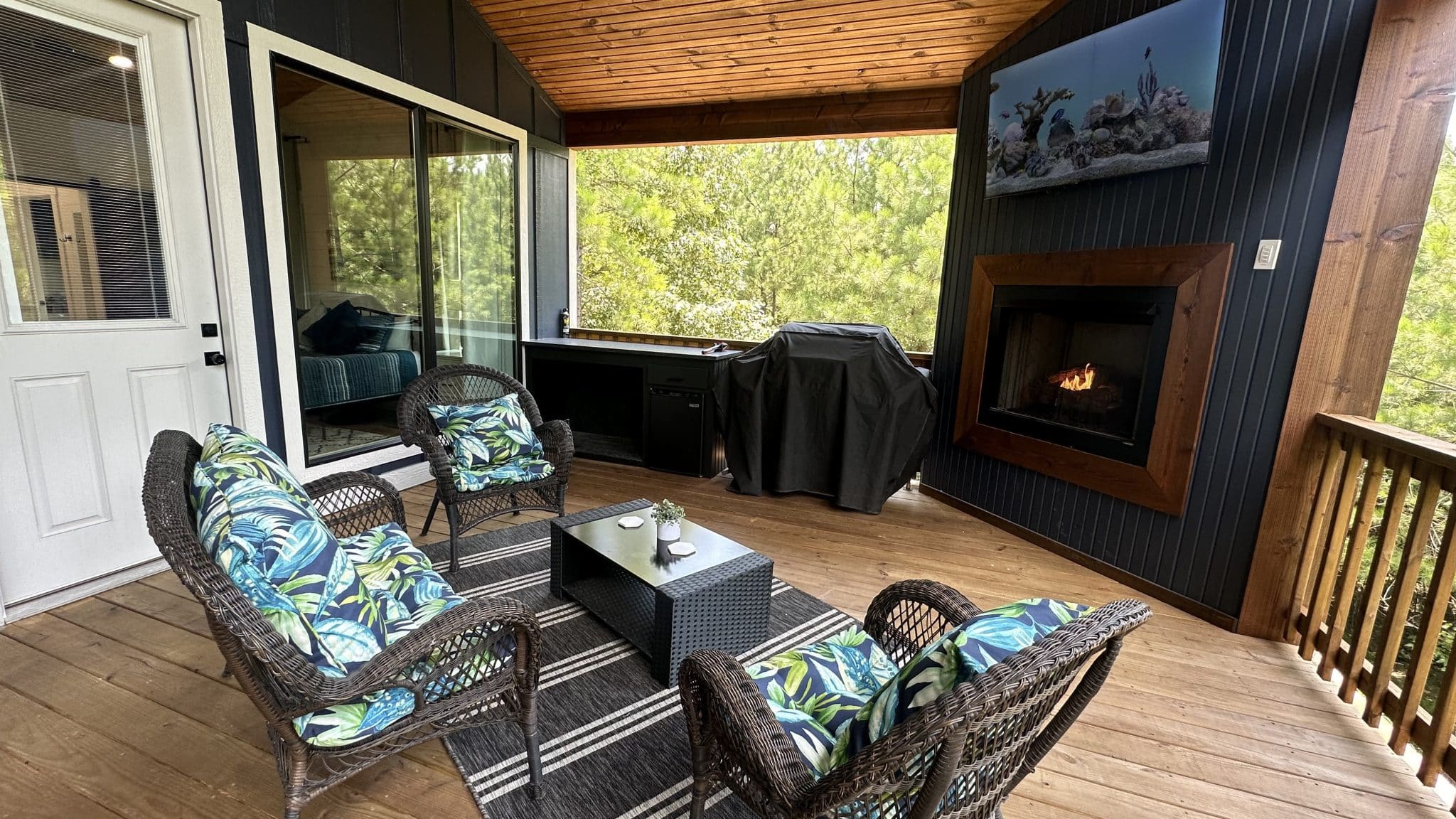 Covered deck lounge with outdoor fireplace, television, grill, and forest views