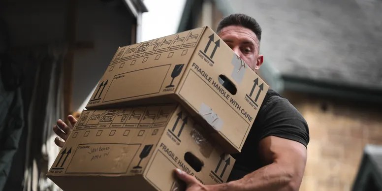 Sean from Bee Smart Removals carefully lifting two labelled cardboard boxes marked "Fragile – Handle With Care" during a house move