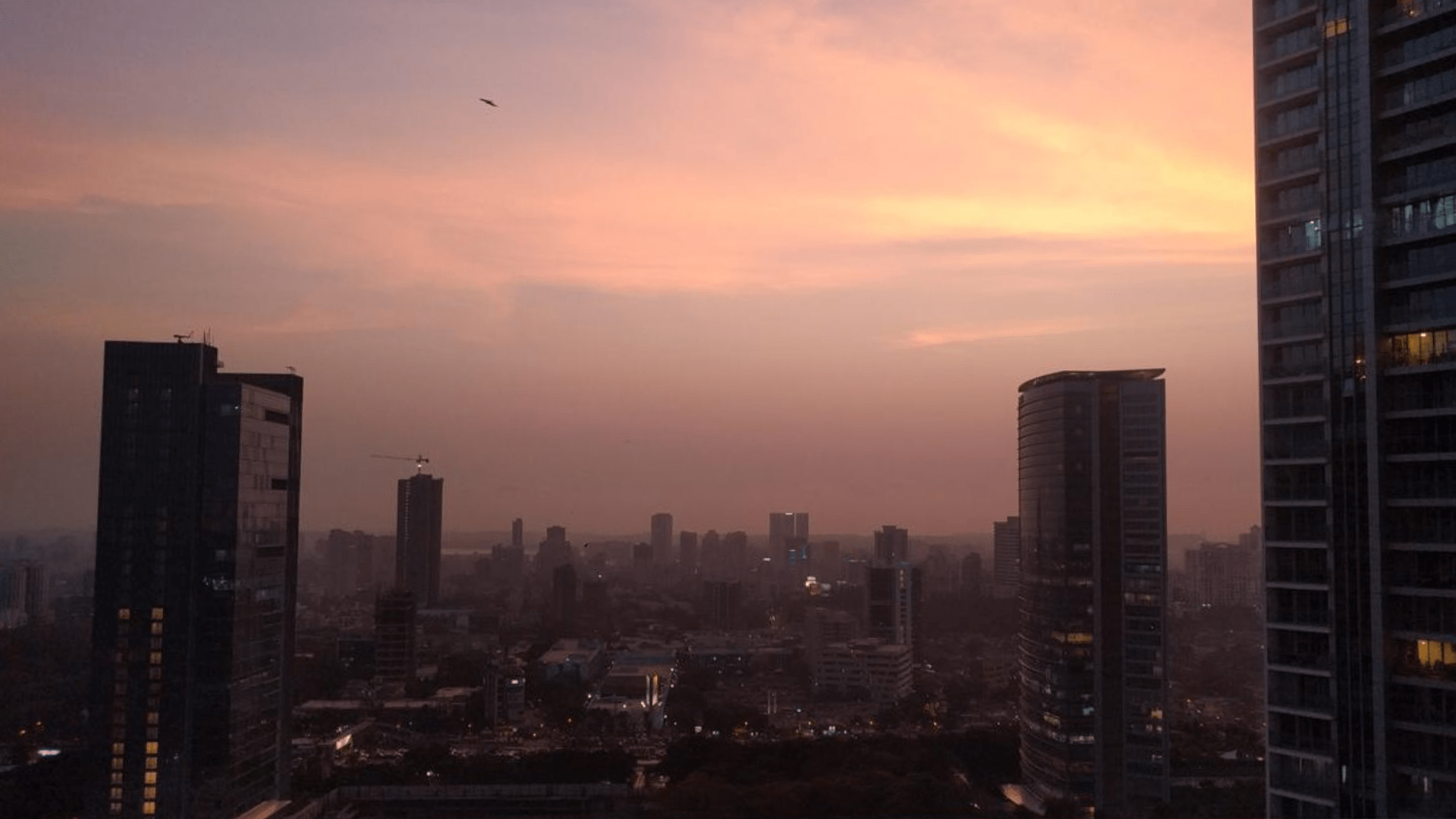 Mumbai skyline at sunset, with high-rise towers overlooking densely packed buildings beneath a pink and orange sky.
