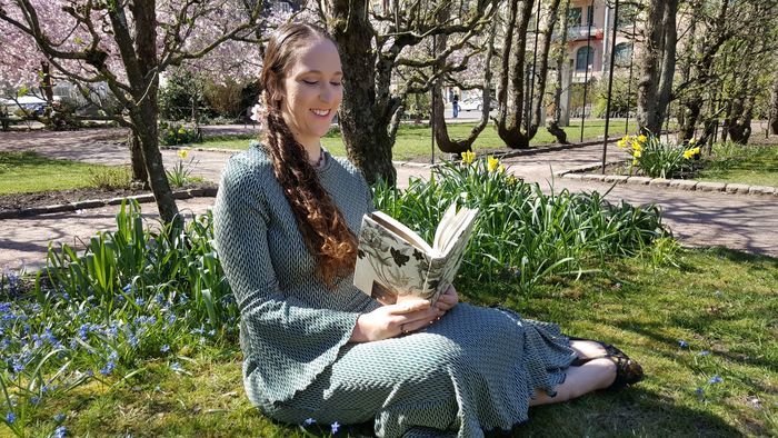 Photo of Astrid V. J. sitting in a park and reading on the grass.