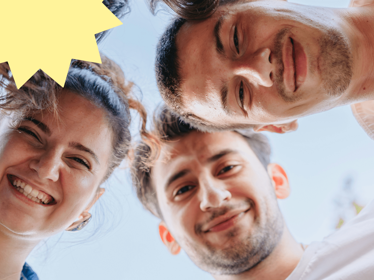 Overhead shot of three young adults leaning in and smiling at the camera, symbolizing warmth and connection for making friends online.