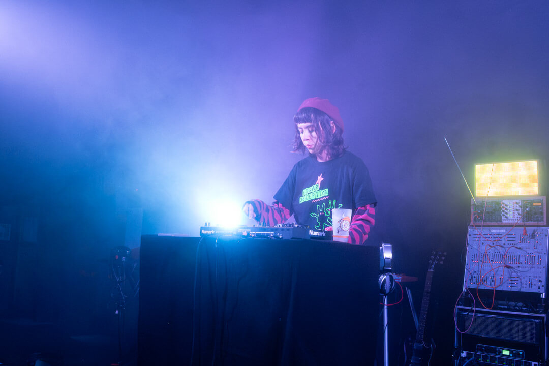 sad echo DJ set at La Bulle Café in Lille, wearing a red beret, with musical electronic equipment and smoke