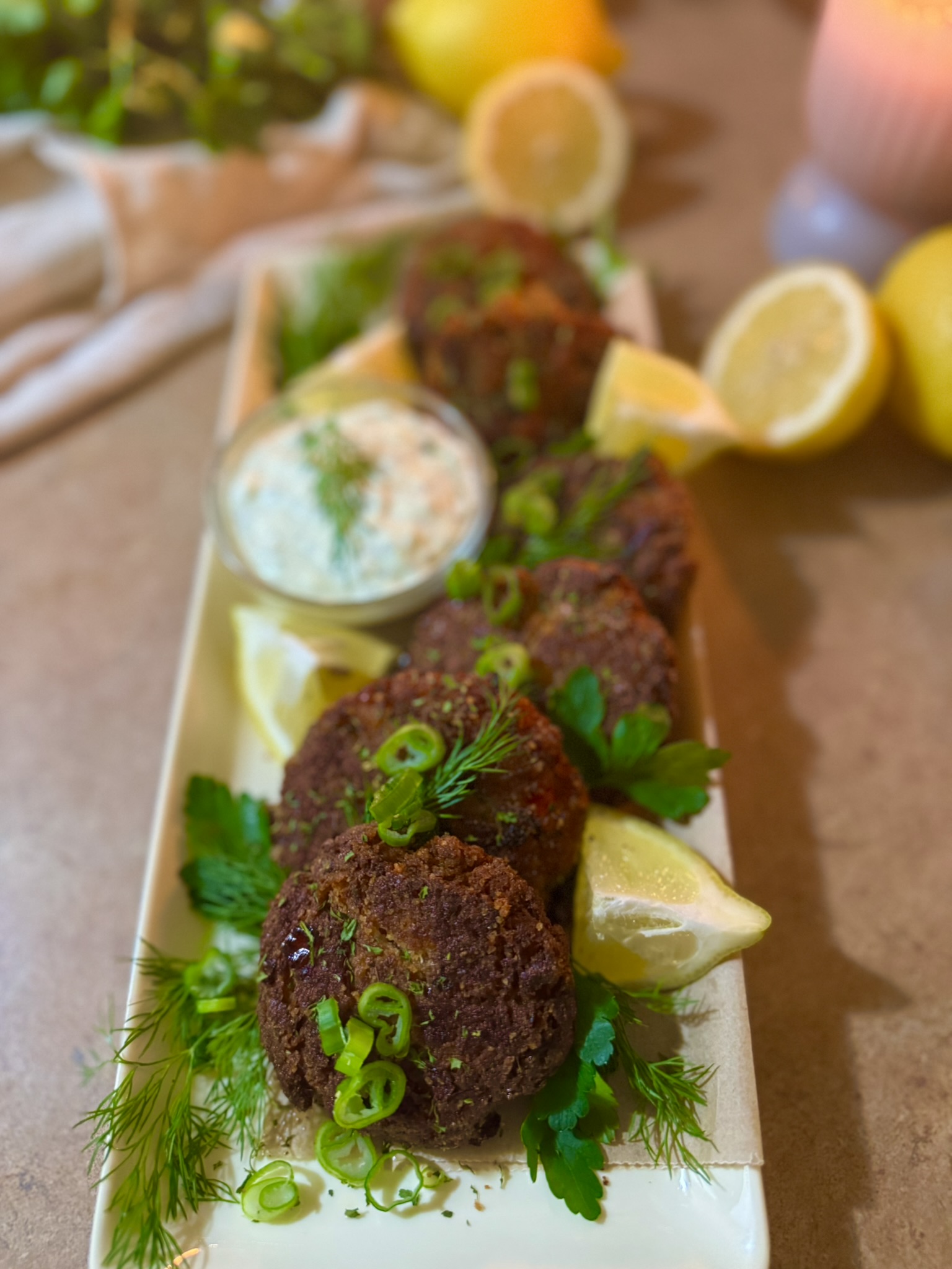 Fresh salmon patties served on a platter with homemade tartar sauce, lemon wedges, and fresh herbs.