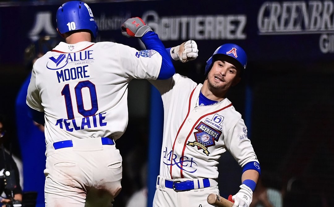 Pelotero con dorsal 10 y nombre Moore celebra en el dugout con un compañero tras conectar un hit, ambos visten uniforme blanco y azul