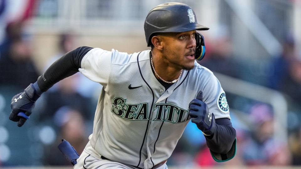 Julio Rodríguez de los Marineros de Seattle corre hacia la base durante un juego, vistiendo uniforme gris de visitante con casco y brazadera azul