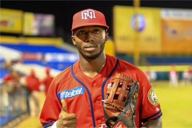 Pelotero con uniforme rojo y gorra roja sostiene su guante de beisbol en el terreno de juego durante la noche