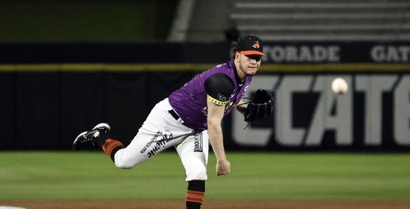 Lanzador de los Rockies en uniforme púrpura y blanco realiza su movimiento en el montículo durante un juego nocturno