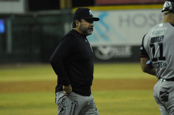 Mánager de los Sultanes en uniforme negro conversa con un jugador de Navojoa durante el partido en el terreno de juego