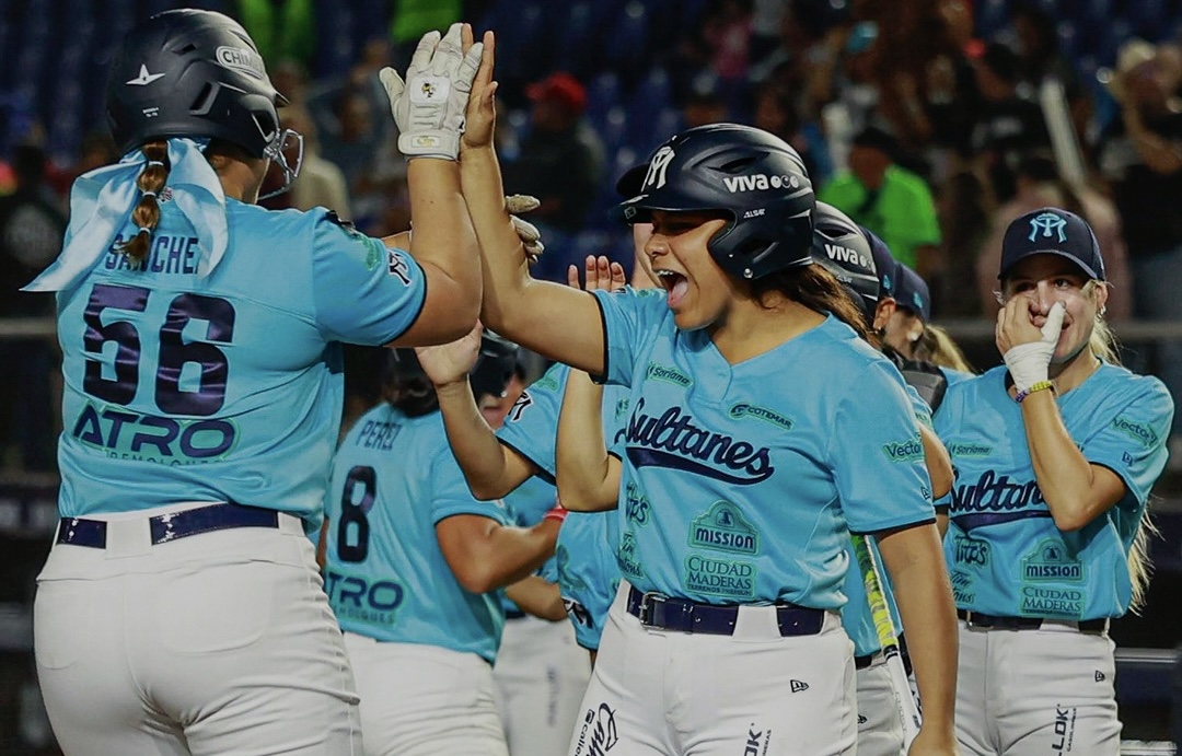 Jugadoras de Sultanes en uniforme turquesa celebran con un high five tras anotar una carrera en el juego
