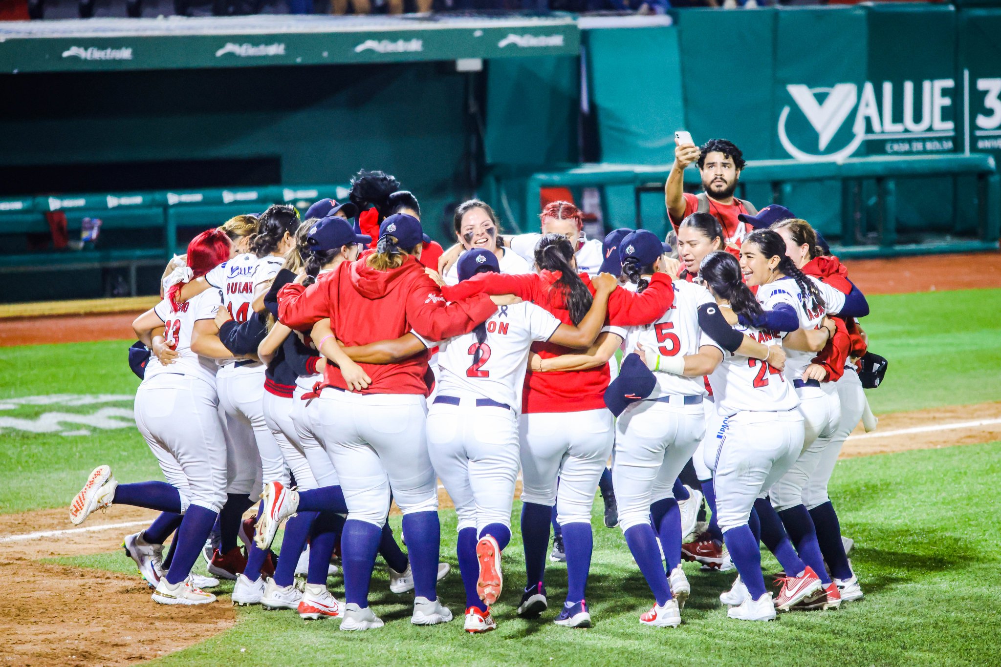Equipo femenino de beisbol en uniforme rojo y blanco con azul marino se reúne en el terreno en celebración durante un partido