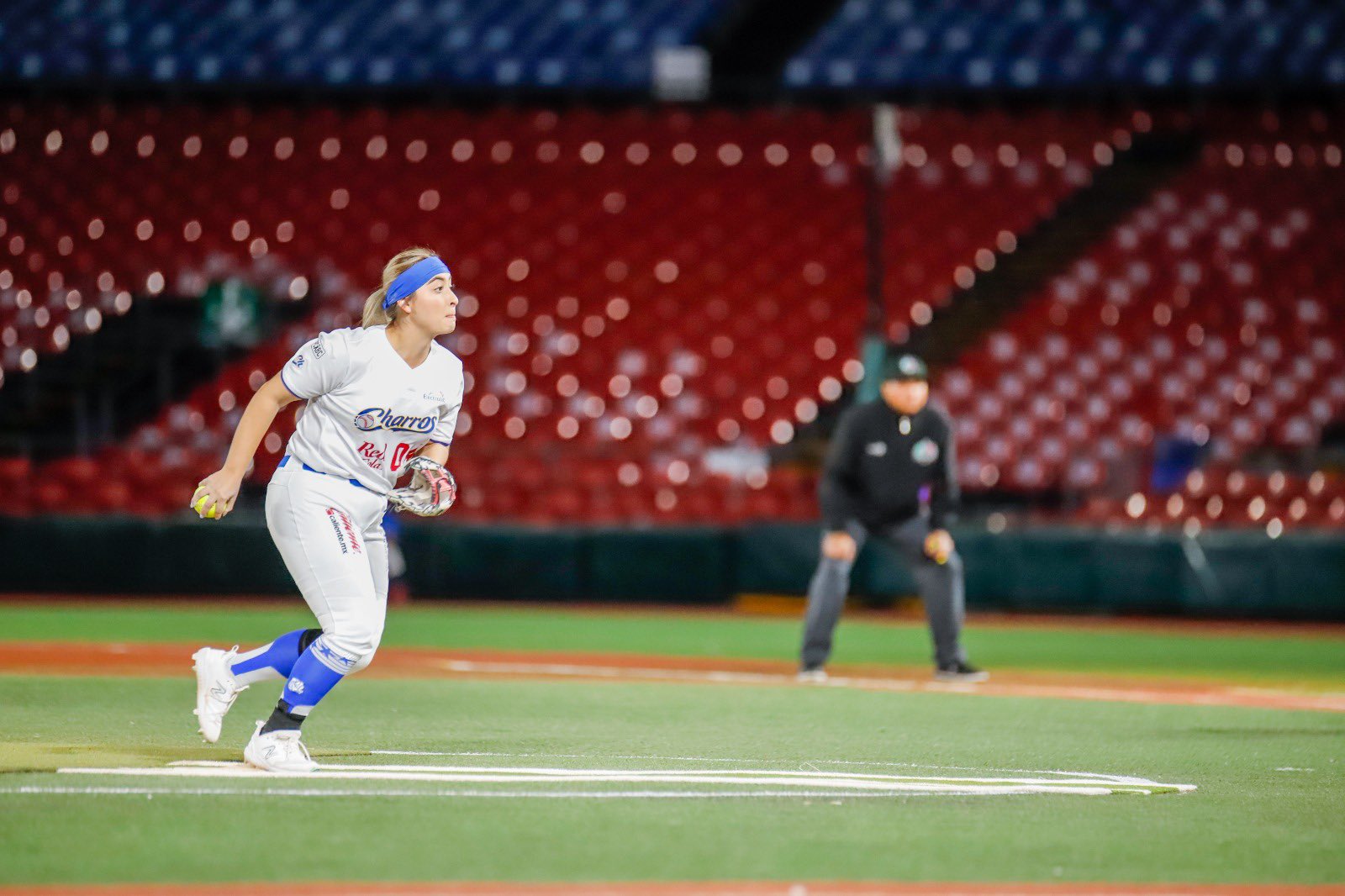 Jugadora de Charros en uniforme blanco y azul corre en la cancha durante un partido de softbol femenil en estadio con gradas rojas